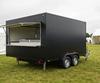 Black twin-axle catering trailer with an open serving hatch at a UK outdoor event