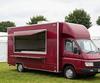 Burgundy box-body burger van with an open serving hatch at a UK event