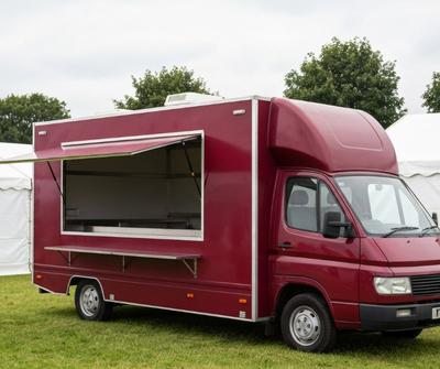 Burgundy box-body burger van with an open serving hatch at a UK event