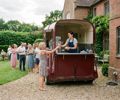 Burgundy horsebox catering conversion serving guests at a UK garden party, hooked up to the house