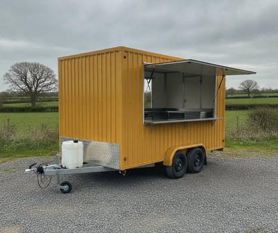 Mustard yellow twin-axle catering trailer with a waste water container by the drawbar