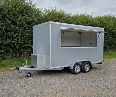 Grey twin-axle box catering trailer with a side serving hatch on a UK pitch