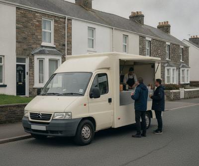 Cream compact catering van with customers at the serving hatch on a quiet dead-end street